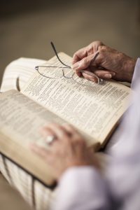 Senior woman reading Bible, holding spectacles, close-up of hands